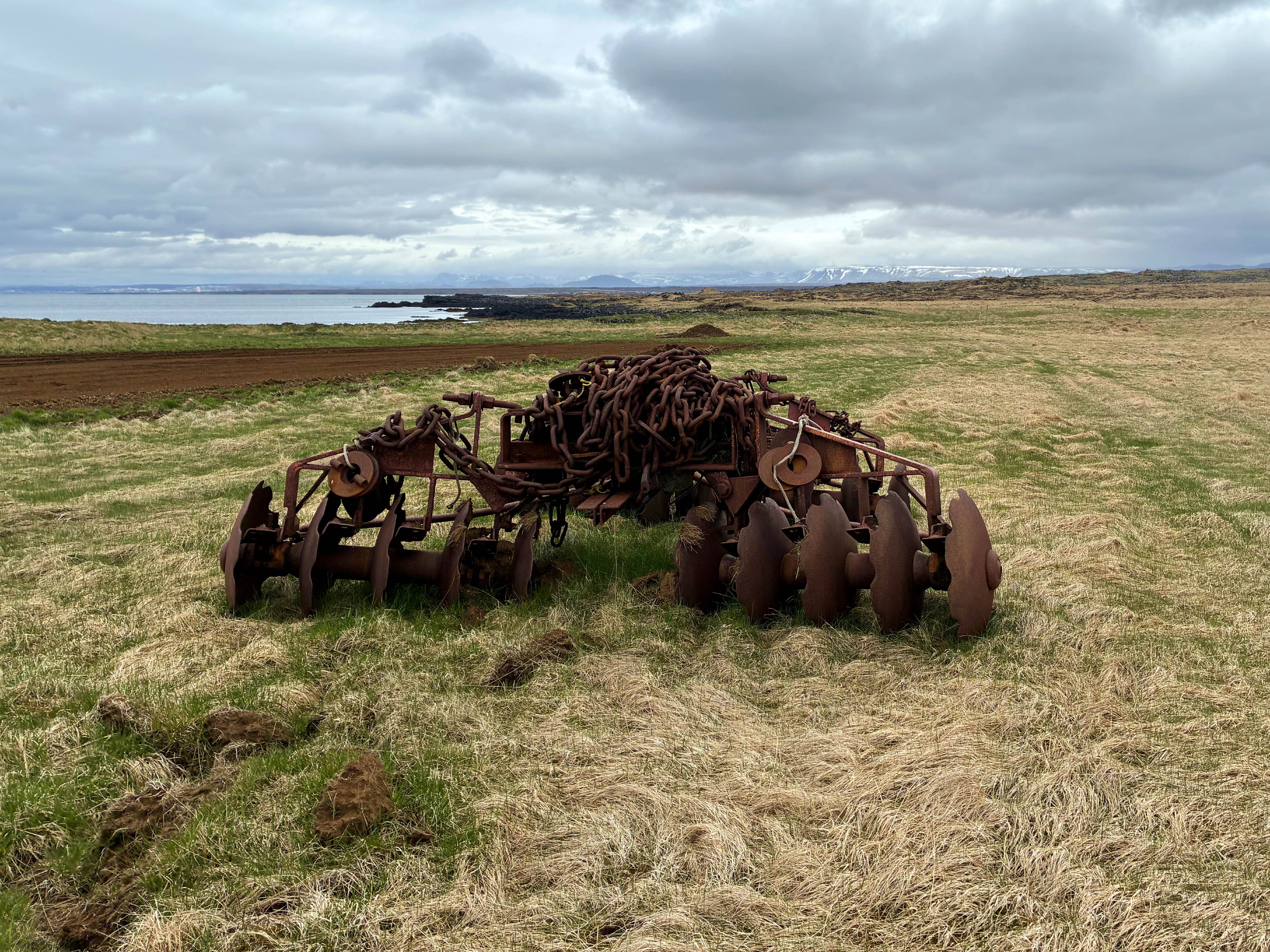 Rusty farm equipment with the ocean in the background.