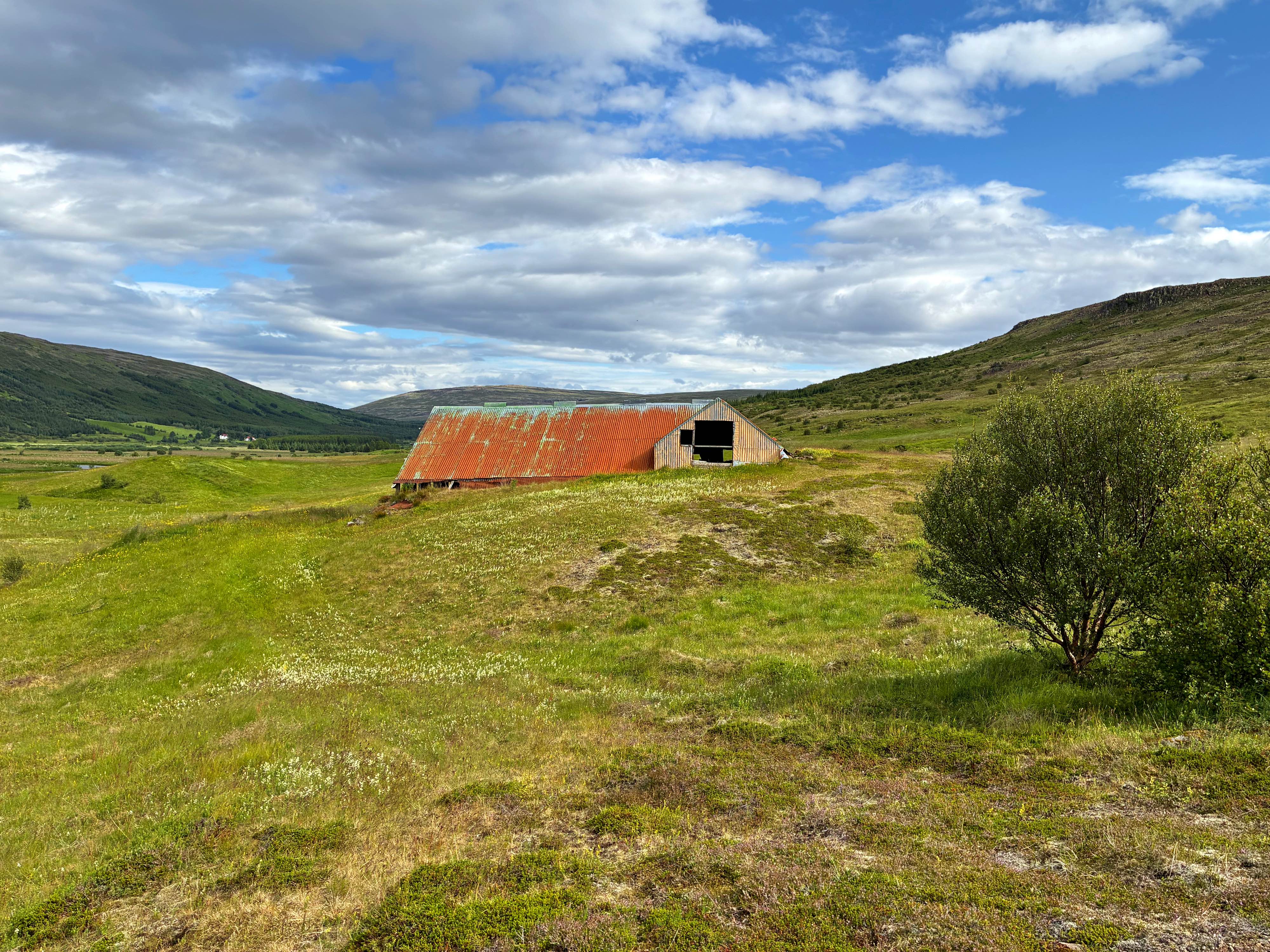 An old barn surrounded by grass and mountains.